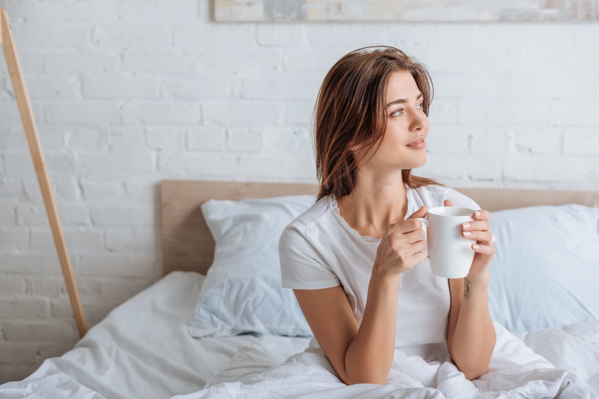 Happy young woman holding cup with tea in be